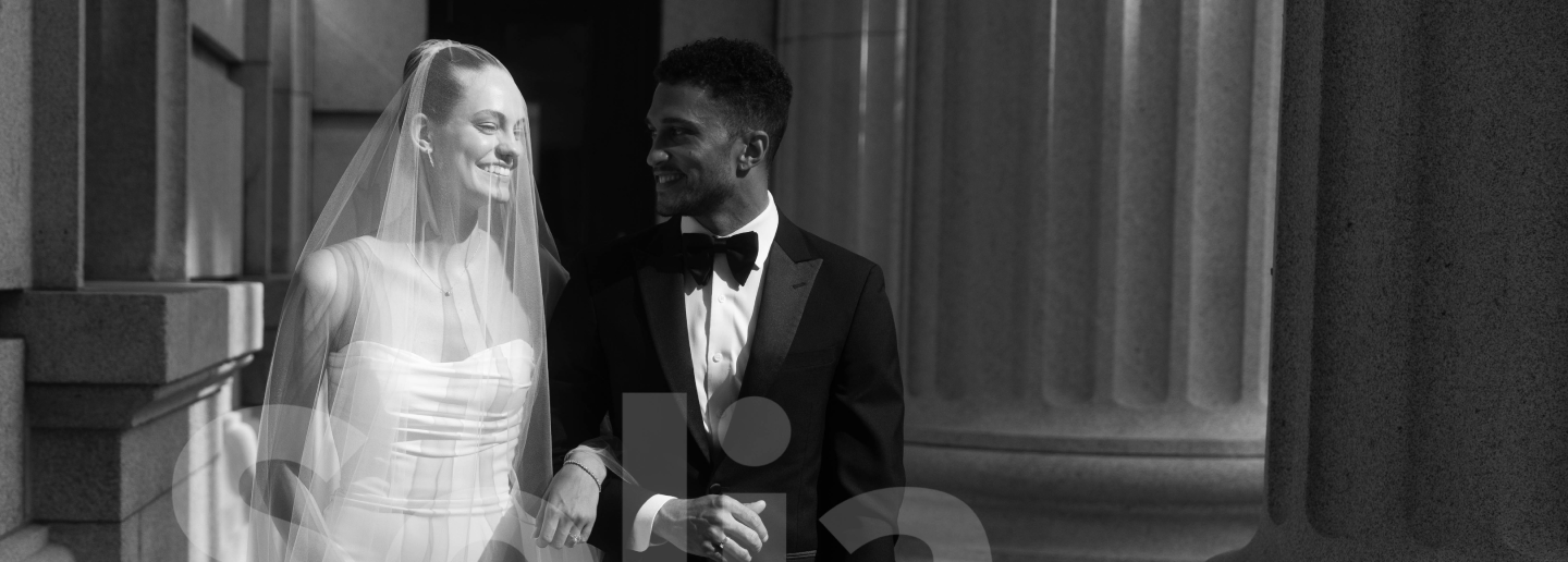 black and white image of bride and groom walking in a hallway with roman pillars