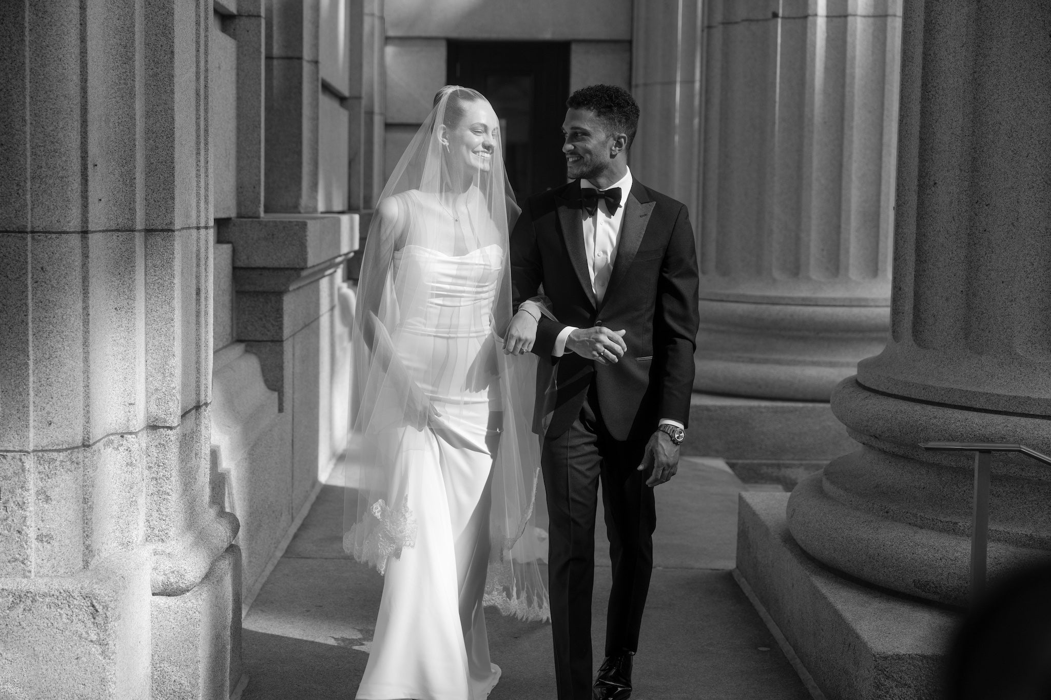 black and white image of a bride and groom walking in a hallway